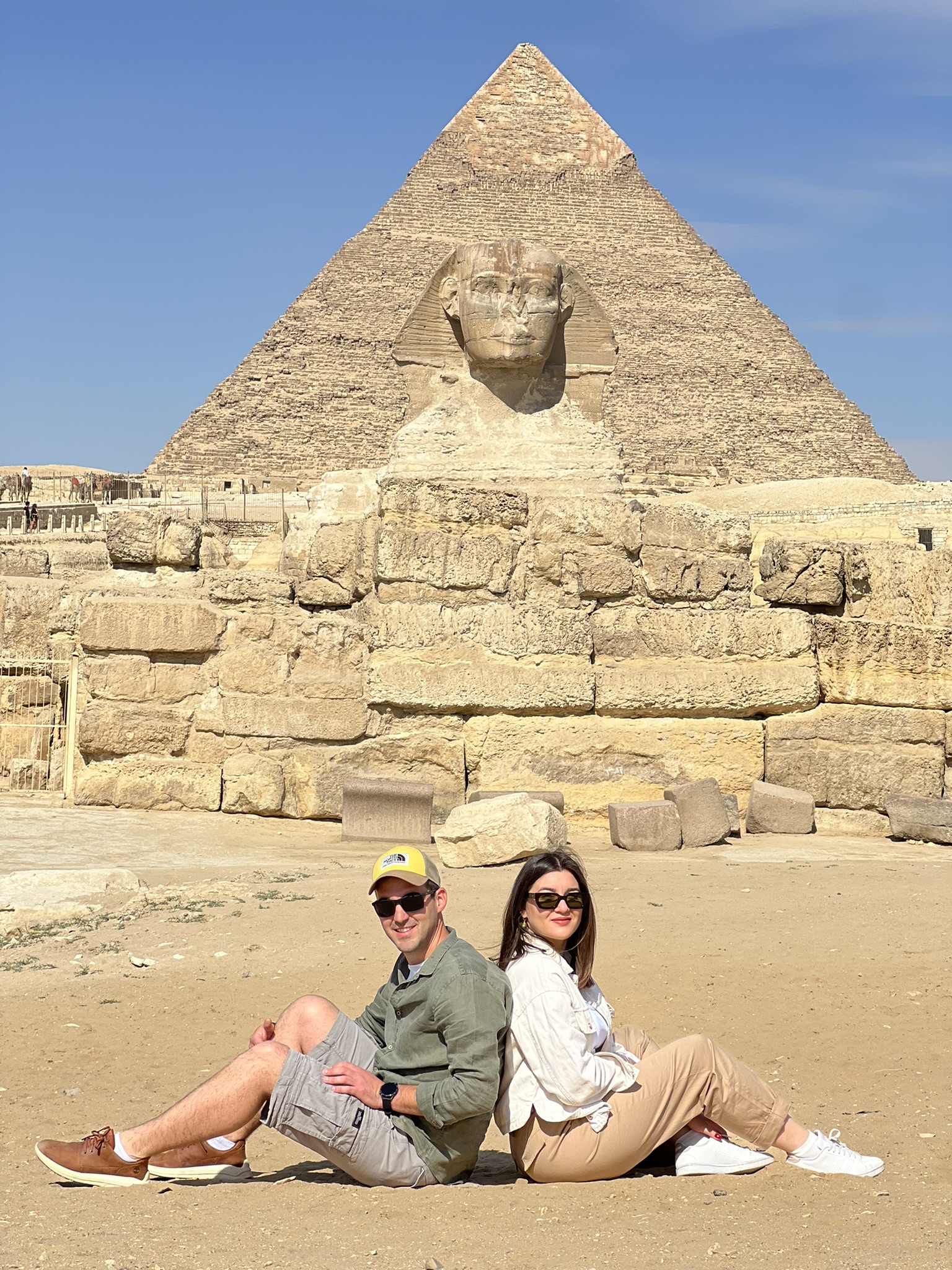 2 persons sitting in from of sphinx and the great pyramids of Giza